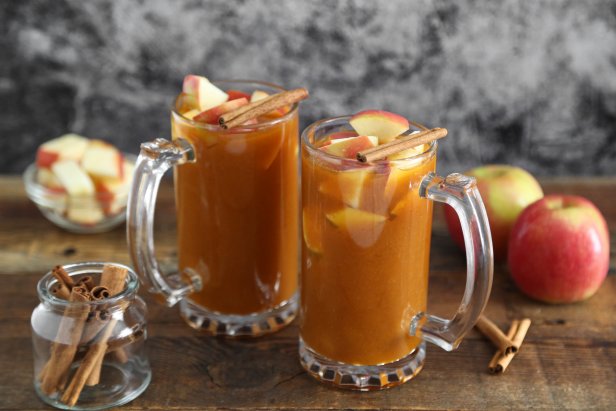 Two Glass Mugs Filled With Pumpkin Spice Apple Cider and Topped With Apple Chunks and Cinnamon Sticks