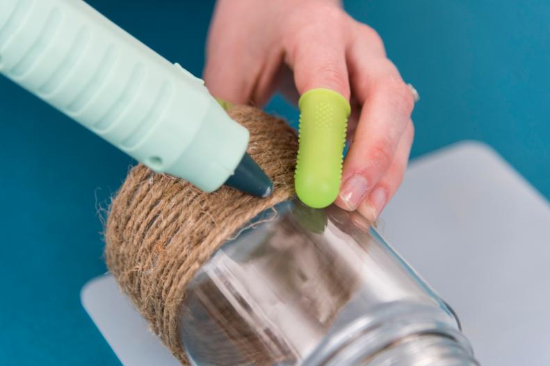 Woman Uses Hot Glue Gun to Affix Jute Around Small Glass Jar