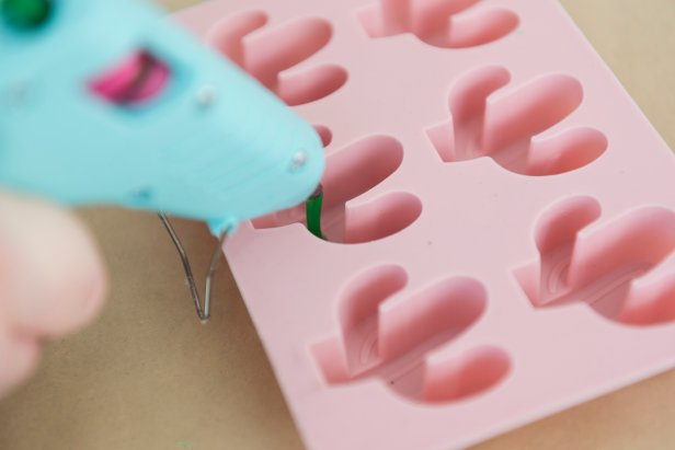 Colored hot glue sticks are super fun to work with. You can make anything from magnets to push pins to necklaces only using glue. You'll need a silicone cactus mold and strawberry mold, some green and pink glue sticks and a low temp hot glue gun to make these really cute push pins. Before you start, make sure your glue gun is very hot. Then, flood the mold with green hot glue for the cactus, or pink for the strawberry. Before the glue dries, place a push pin in the middle of the mold with the pin facing outward. Once dry, add a mini pompom with a clear hot glue stick to the cactus, or draw on strawberry seeds with a black permanent marker. Once dry, enjoy!