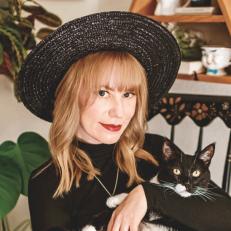 Woman Wears Witch Hat, Holds Black Cat, Smiling To Camera