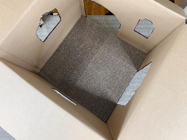 Once the box is dry, add cat scratch pads to the inside of the box. Close the lid of the box and tape it shut. Add hot glue to the top of the box and place the scratch pads on top. Tip: If the scratch pads are too large to fit, cut them down to size by scoring them with a craft blade or box cutter.