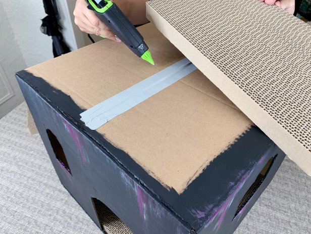 Once the box is dry, add cat scratch pads to the inside of the box. Close the lid of the box and tape it shut. Add hot glue to the top of the box and place the scratch pads on top. Tip: If the scratch pads are too large to fit, cut them down to size by scoring them with a craft blade or box cutter.