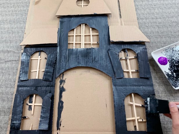 Add a base coat of black acrylic paint to the house making sure to get all the nooks and crannies. While the paint is still wet add texture by mixing in different colors and sloppily painting them on. Tip: Drag a semi dry brush down from window edges and roof tops to create a weathered look.