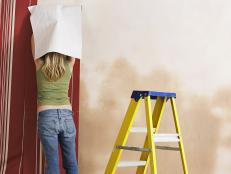 Woman Hanging Wallpaper Is Unable To Get It On The Wall Alone