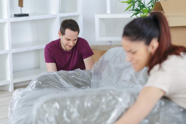 Man And Woman Cover Furniture With Plastic In Room With Bookshelves