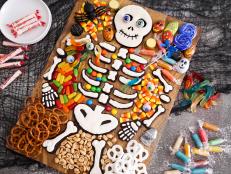 Frighten up your Halloween party table with this scary-cute skeleton bone cookie board. The spaces between the cookies overflow with sweet and salty treats to create an interactive, crowd-pleasing dessert display.