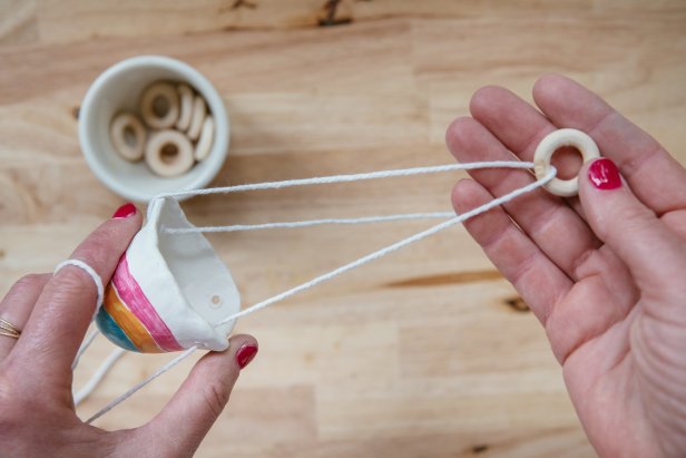 Use cotton twine and small wooden rings to hang the pot (Image 1). Thread twine through the first hole and then through the wooden ring (Image 2). Then, thread through the second hole and back through the wooden ring (Image 3). Repeat again with the third hole and tie off to the beginning of the twine (Image 4).