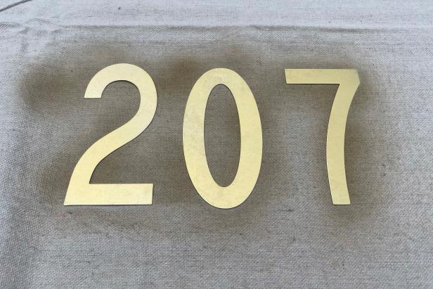 Arrange plain metal house numbers on a crafting table. Use gold spray paint to dress up the numbers, giving each side a coat of paint. Let dry completely.
