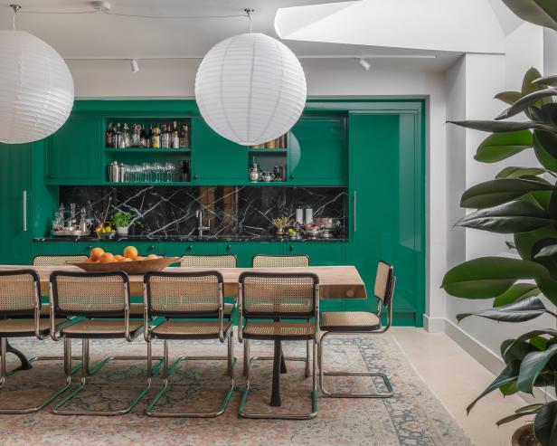 A wooden dining table in front of green kitchen cabinets