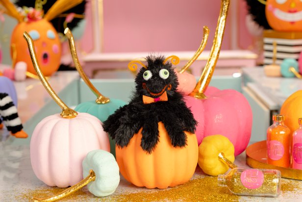 Handmade, smiling spider hand puppet sits on top of pastel pumpkins