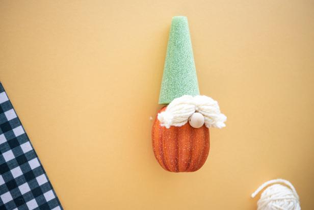 The yarn eyebrows for the DIY pumpkin gnome are made with a bundle of looped yarn secured with three ties — one in the center and one on each end. The eyebrows for this easy fall craft project are hot glued to the pumpkin just above the wooden bead nose.