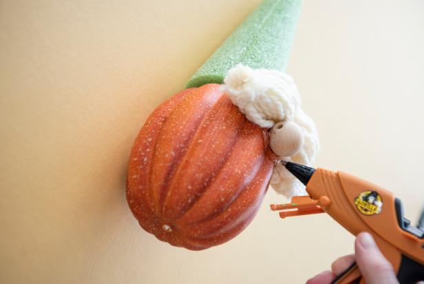 The gnome pumpkin's yarn beard is secured to the pumpkin by using a generous amount of hot glue. Attaching the beard is the last step of creating the DIY gnome's face before moving on to the final two steps — finishing the hat and attaching the pumpkin to the wooden base.