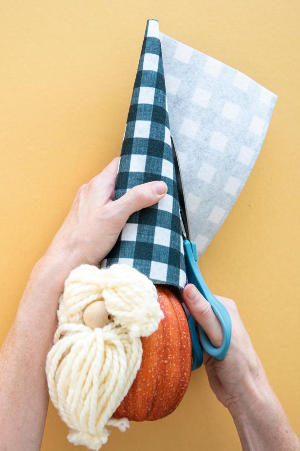 The no-carve pumpkin gnome's hat is created by wrapping fabric around a floral cone, trimming the excess and securing it with two strips of hot glue. Customize your gnome by selecting your favorite fabric print for the hat and different colors for the yarn eyebrows and beard.