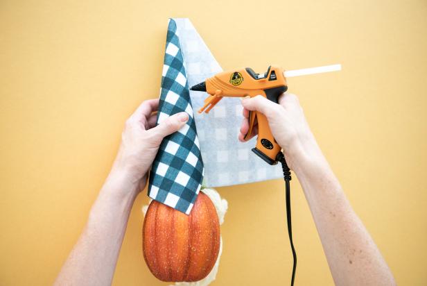 The no-carve pumpkin gnome's hat is created by wrapping fabric around a floral cone, trimming the excess and securing it with two strips of hot glue. Customize your gnome by selecting your favorite fabric print for the hat and different colors for the yarn eyebrows and beard.