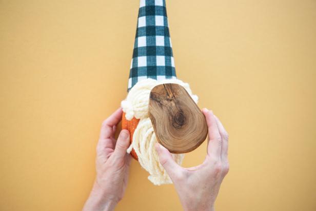A wooden disk serves as the base for the no-carve gnome pumpkin. After the face and hat are complete, the pumpkin is glued to the disk. Customize the pumpkin gnome by changing the hat fabric or the yarn color, or consider painting or staining the wooden disk.