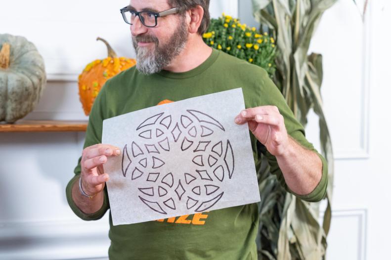 Man Holds Up Tracing Paper Pattern That Will Go Onto The Pumpkin