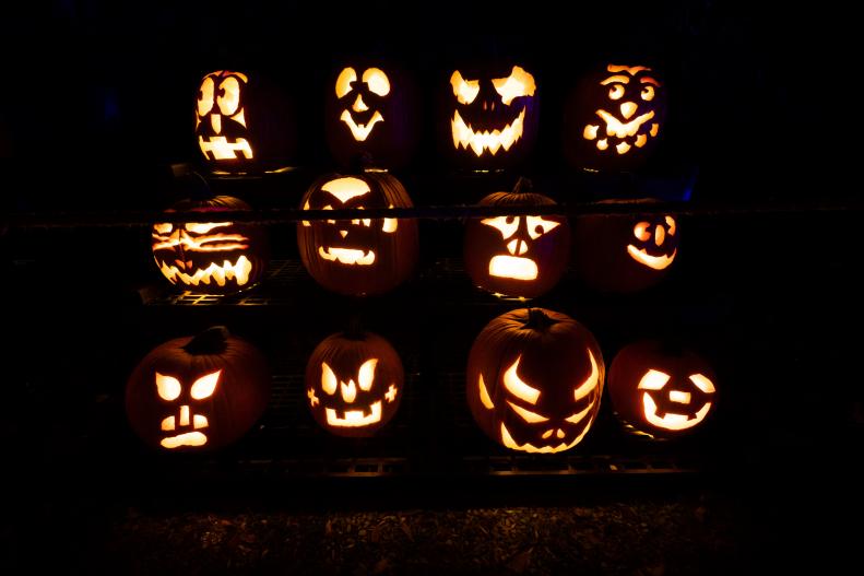 Carved Glowing Pumpkins With Creepy Faces Stacked Together at Night