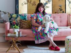 Bari Ackerman sits on a pink couch holding a white Goldendoodle.