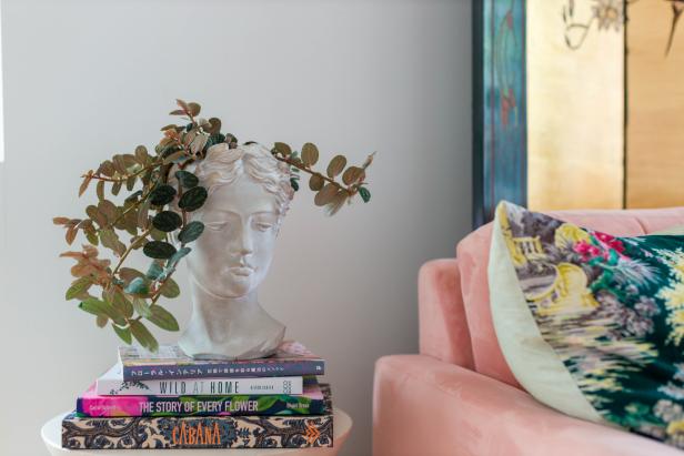 A leafy plant grows out of a Greek statue bust planter on a side table