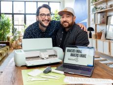 Two men stand in office with cutting machine, laptop and tools on desk