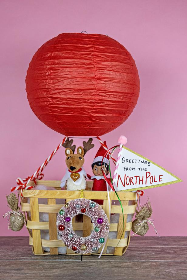 A toy elf and stuffed moose in a wooden basket below a paper lantern