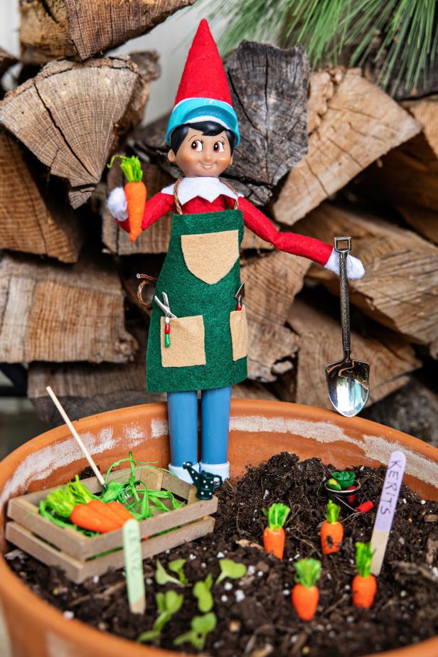 A toy elf in an apron holds a shovel and a felt carrot.
