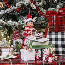 A toy elf poses with several small, wrapped Christmas presents.