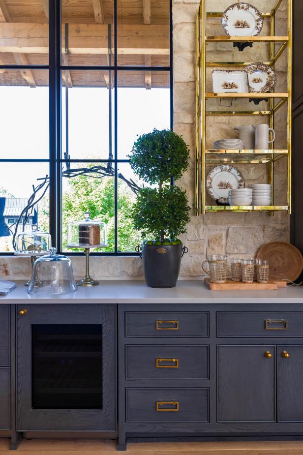 Limestone kitchen with grey cabinets and brass floating shelves.