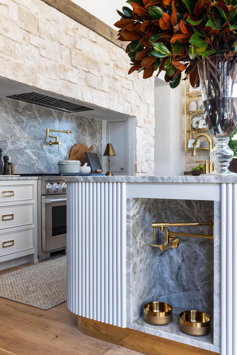 White fluted kitchen island with stone-lined niche and brass bowls. 