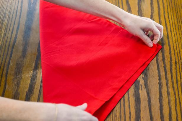 Step one of this Christmas bow napkin fold is to fold the napkin in half to form a triangle.