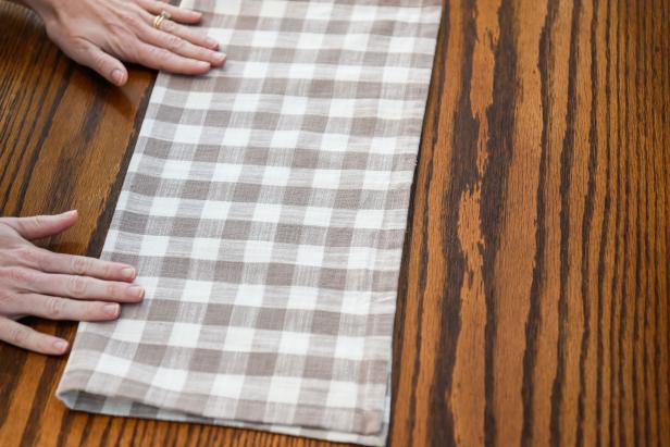 To begin this DIY Thanksgiving cornucopia napkin, fold a napkin in half.