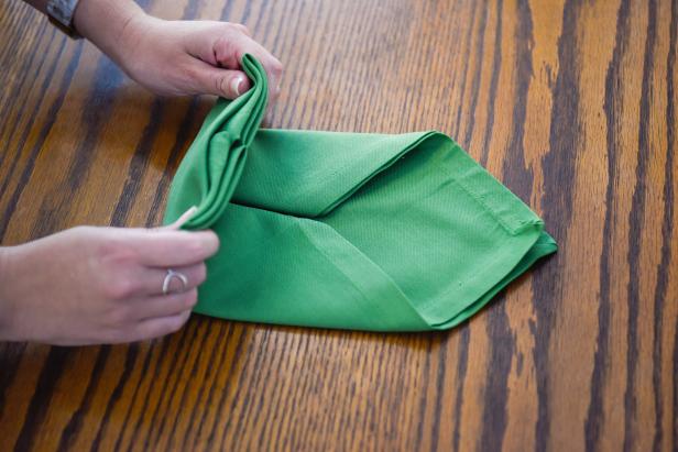 Continue forming the envelope-shaped napkin by folding the bottom portion upward.