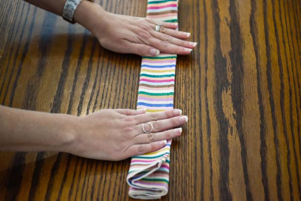 The next step in turning a cloth napkin into a Christmas gift is to accordion fold the napkin into a long strip.