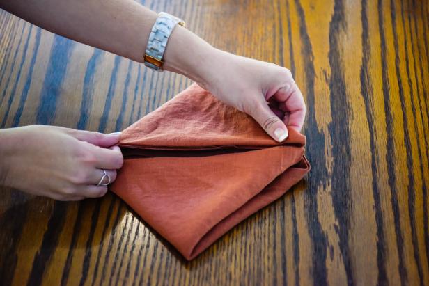 The next step in creating this Thanksgiving leaf napkin is to fold the bottom corners upward to the middle.