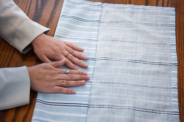 The first step in folding this napkin into a holiday star is to fold the top and bottom flap toward the middle.