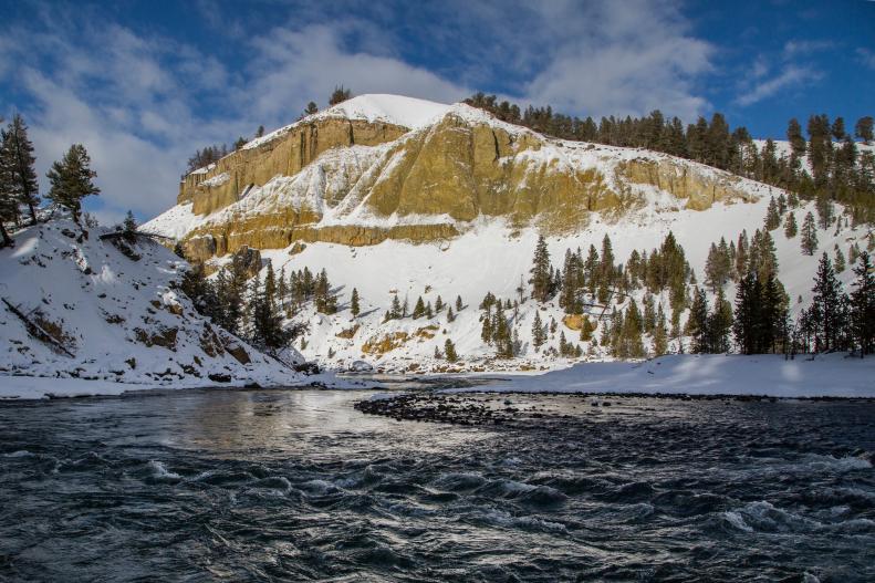 A view of the Yellowstone River in Yellowstone National Park, with snow-capped mountains surrounding it.