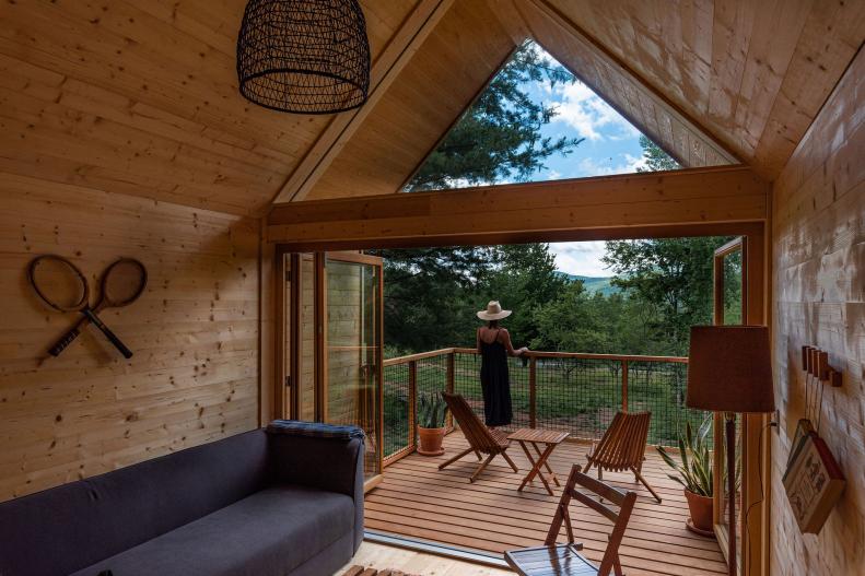 Pine paneled cabin with glass wall and dark sofa. 
