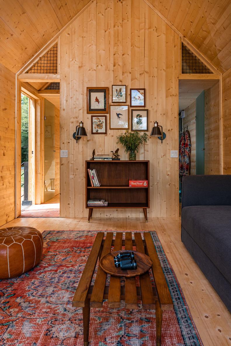 Pine paneled room with wood dresser, framed prints and red rug.