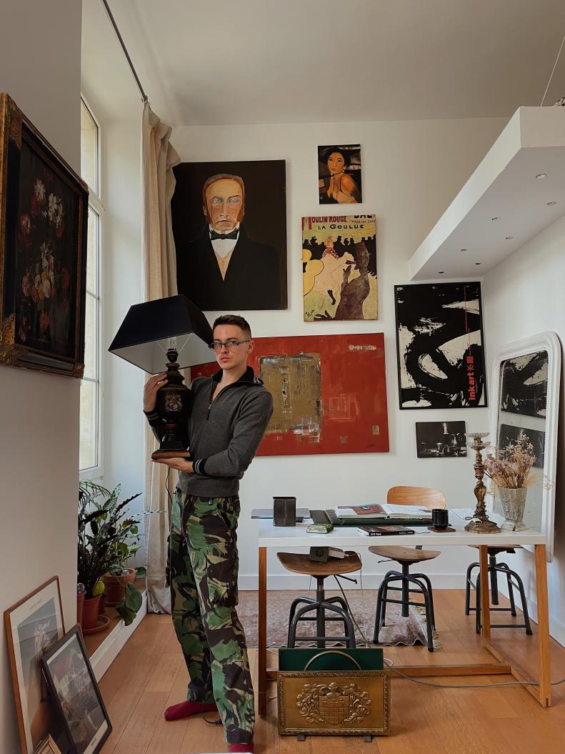 A man, Damon Dominique, holds a lamp in front of his gallery wall