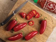 Slices of jalapeno pepper 'Sriracha' resting alongside a knife on a cutting board