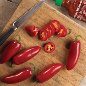 Slices of jalapeno pepper 'Sriracha' resting alongside a knife on a cutting board