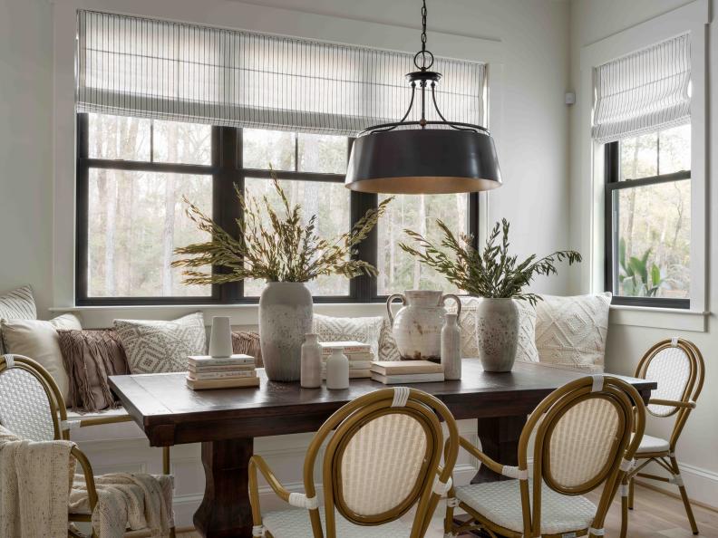 A transitional-style chandelier with dark bronze exterior casts a lovely glow over this casual and stylish dining space for sharing meals, with spacious wood dining table and woven bistro arm chairs that bring a coastal vibe.