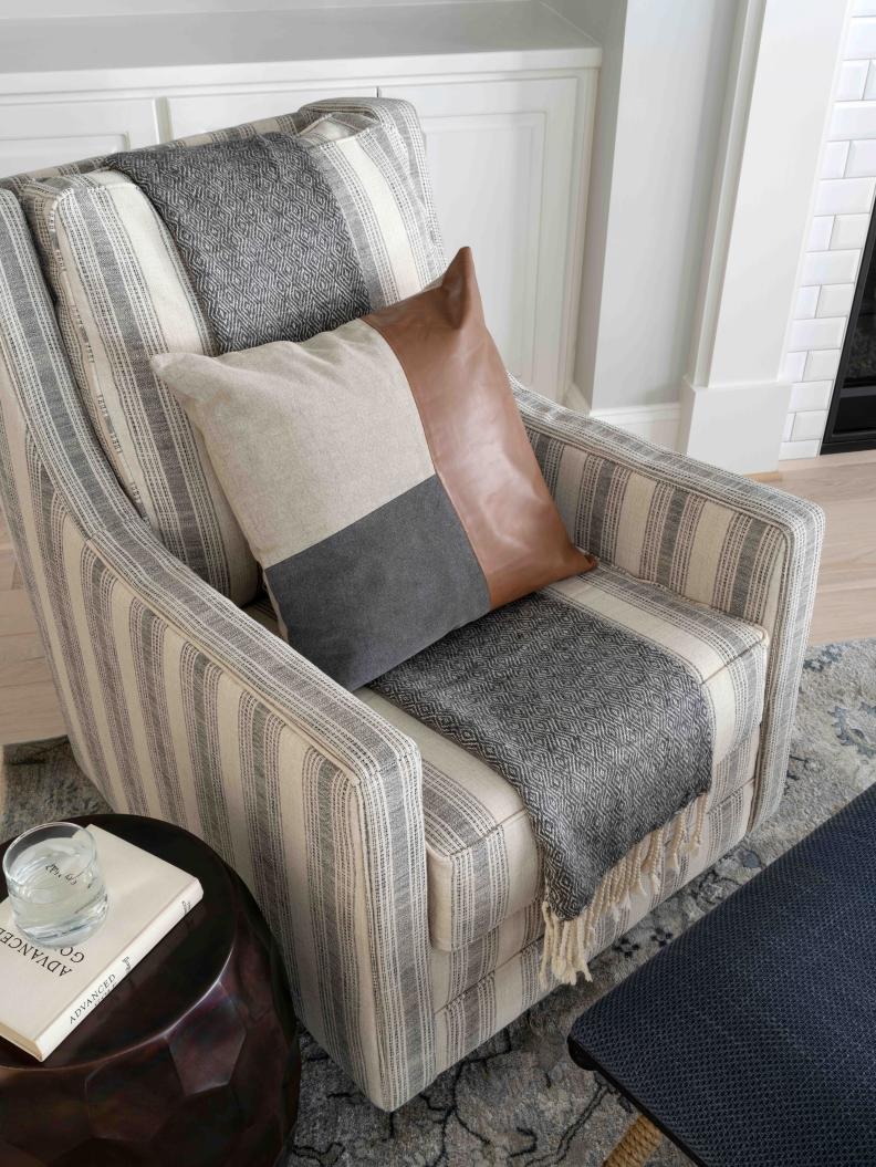 The on-trend accent chairs have a sloped arm design, metal slider base, reversible cushions, and polyester upholstery in an ivory and black striped pattern. Leather pillows and cozy throws add extra comfort to each chair.