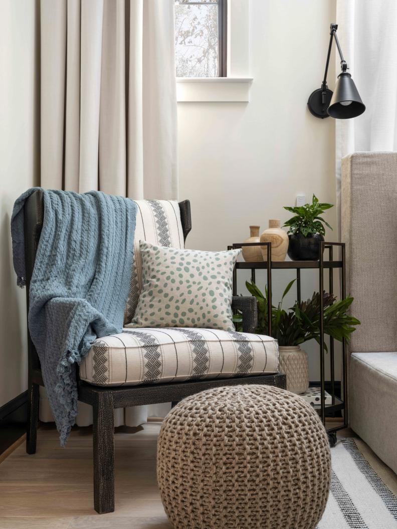 A global-chic accent chair for reading by the bed has a sturdy wood frame with distressed black finish, and reversible foam cushions covered with an ivory and black tribal pattern. A chunky hand-knitted pouf with the chair offers a way to put up your feet, or use as a small extra seat.