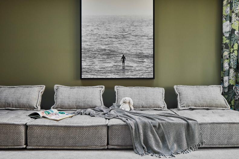 A large sofa in the playroom provides room to unwind while curling up with books and magazines. Large format artwork depicting a local coastal scene anchors the adjacent wall and brings a sense of place to the soothing space.