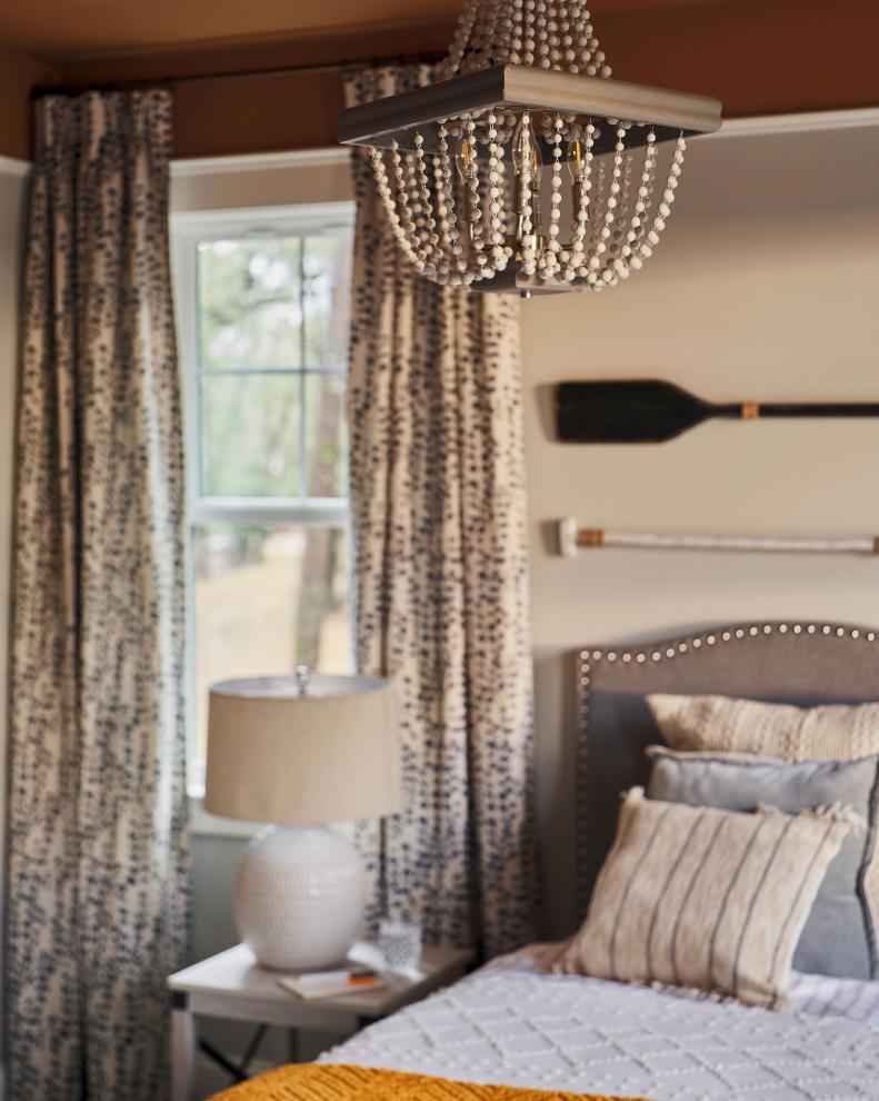 Layering textures throughout the guest bedroom keeps the eye moving and gives the space a luxurious feel. Wooden beads on the chandelier play off the metallic, round nail heads on the upholstered headboard while a geometric knit blanket and wooden oars above the bed add warmth with coastal cottage charm.  