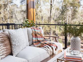 An outdoor sofa in a soft neutral upholstery gets a dash of color with textured pillows and a striped throw. Potted plants bring an element of nature into the seating area while clear panels with modern railings highlight the outstanding views.