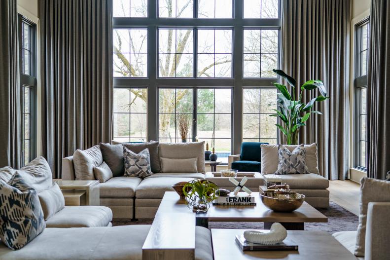 Tan living room with low seating and massive window with forest view.