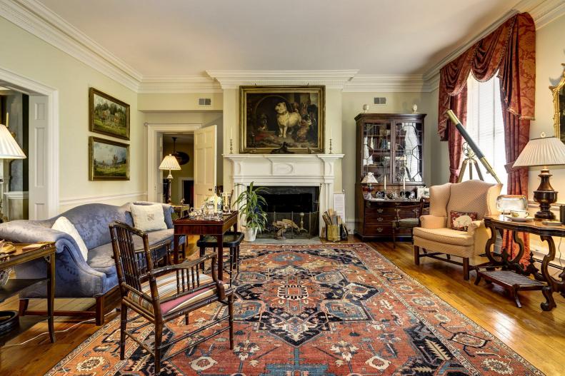 Sitting room with oil paintings and large Persian rug near fireplace.