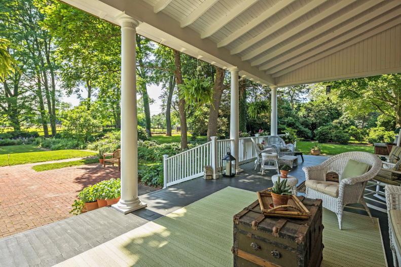 Covered porch with white wicker furniture and view of tree-lined yard.